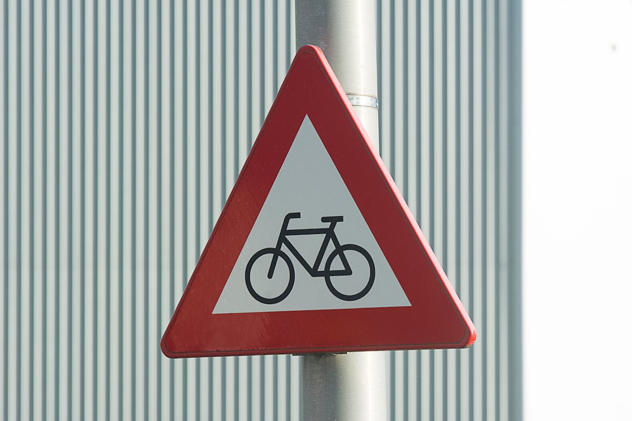 Red triangular bicycle warning road sign against a striped metal background, indicating bicycle path.