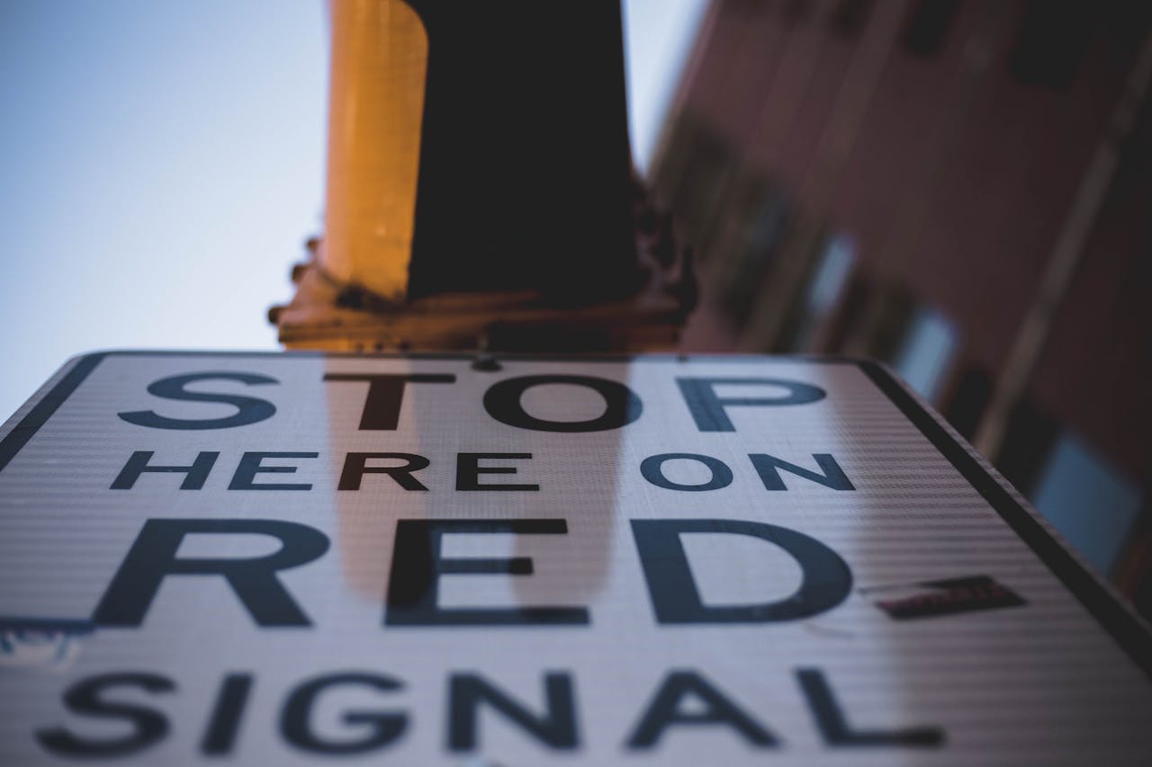 Low angle shot of a 'Stop Here on Red Signal' sign emphasizing urban traffic guidance.