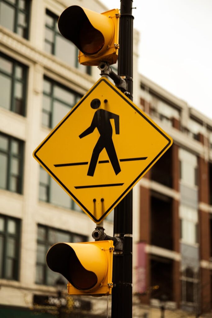 Yellow pedestrian crossing sign with traffic lights in a city setting.