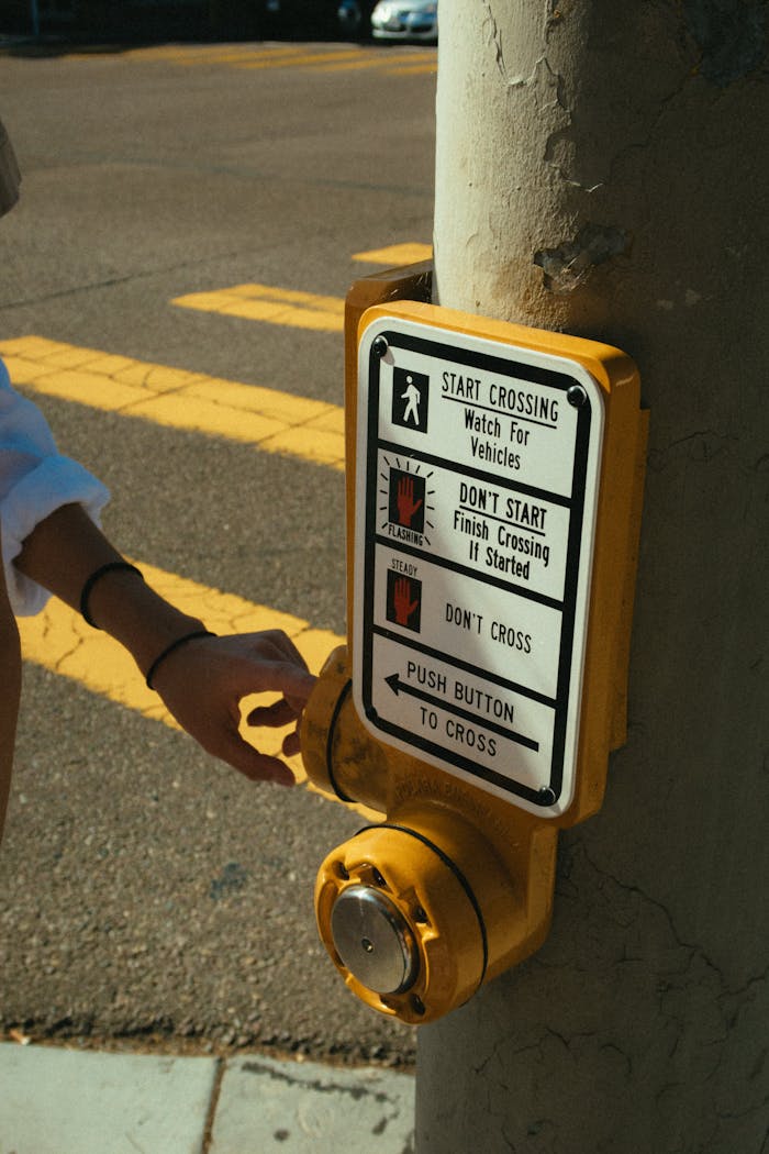 Person pressing crosswalk button on sunny day for street crossing.